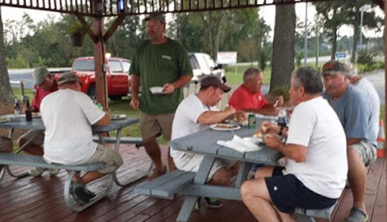 Group of guests dining together at picnic tables under a pavilion at Sportsman Inn
